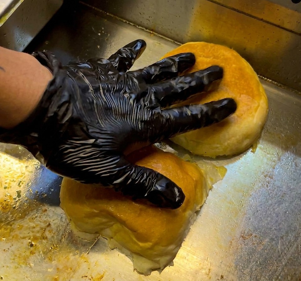 Un hamburger di manzo crudo e condito posizionato sulla superficie rovente di una piastra.