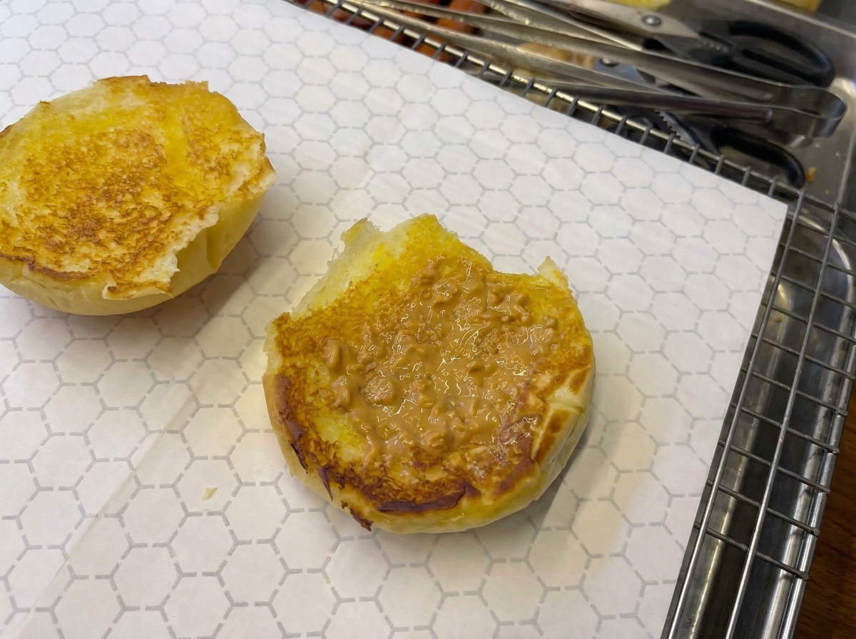 Primo piano di un panino con la salsa che viene leggermente fiammeggiata con un cannello da cucina.