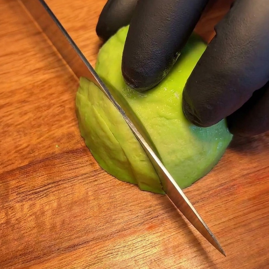 Fette sottili e uniformi di avocado fresco disposte su un tagliere.