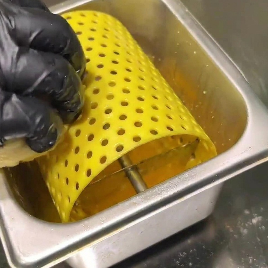 Hamburger di manzo crudi che sfrigolano su una piastra calda, premuti da una spatola.