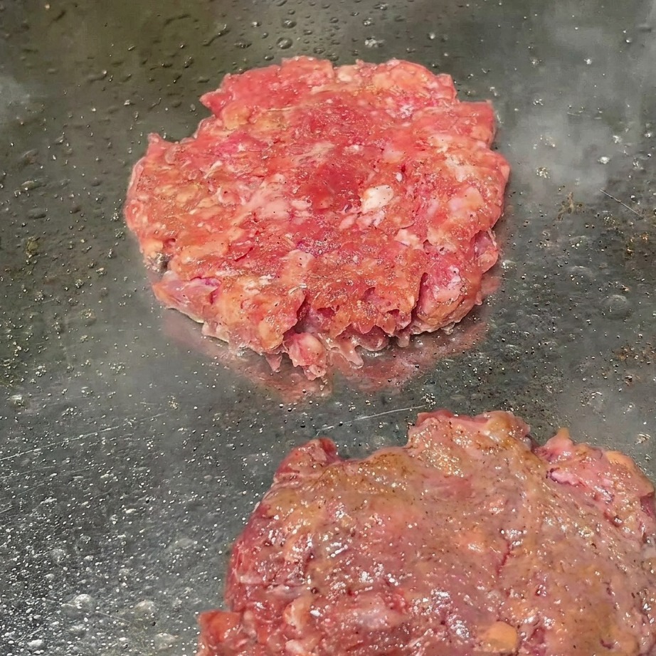 Hamburger di manzo sulla griglia mentre vengono spolverati con pepe nero macinato fresco.