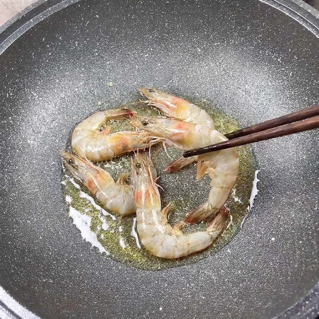 Gamberi che cuociono in padella, girati con le bacchette.