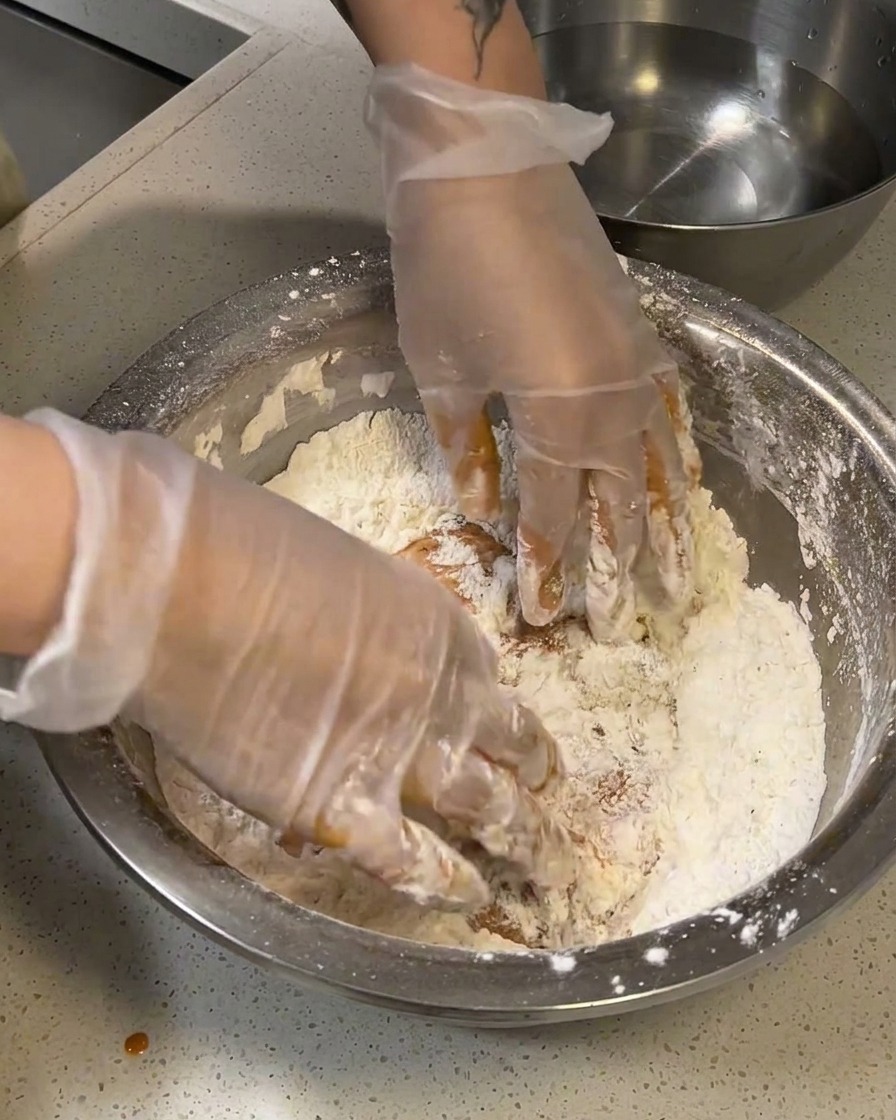 Pollo crudo marinato pressato con decisione in una ciotola contenente il mix di farine.
