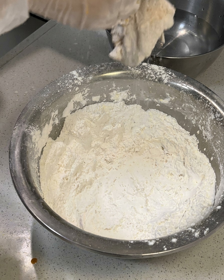 La sovracoscia di pollo panata viene delicatamente ricoperta di altra farina per creare una crosta texturizzata a scaglie.