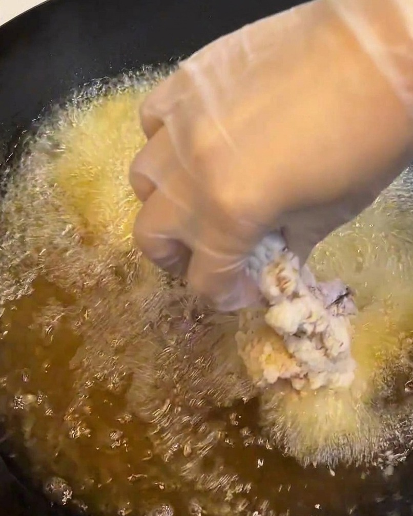 Una sovracoscia di pollo panata immersa in una padella di olio caldo e scoppiettante.