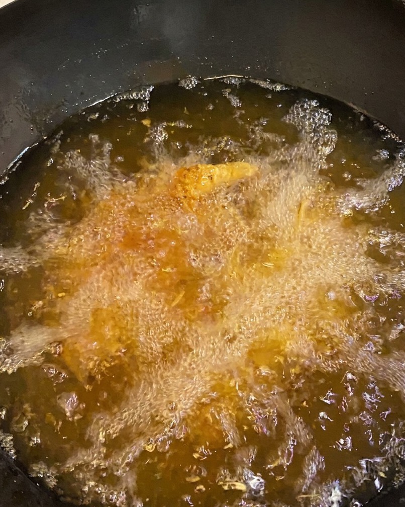 Sovracosce di pollo che friggono in abbondante olio, mostrando una crosta dorata e intensa.