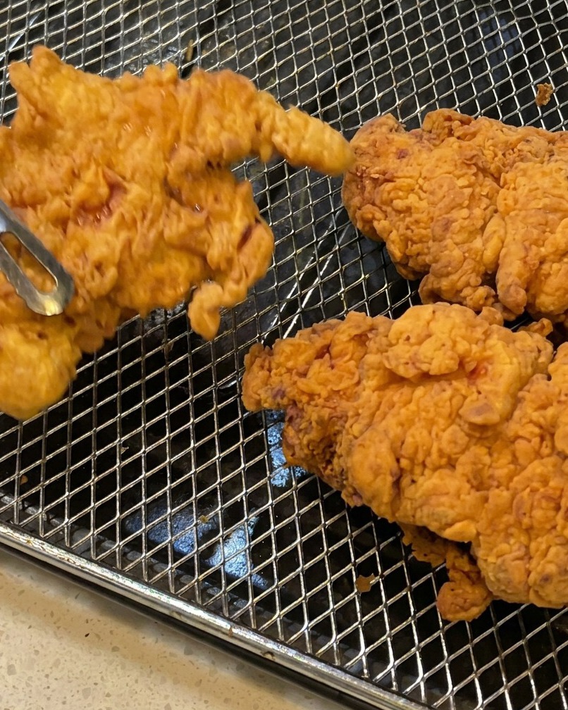 Sovracosce di pollo fritte estratte dallolio con pinze di metallo, con in evidenza la panatura a scaglie.