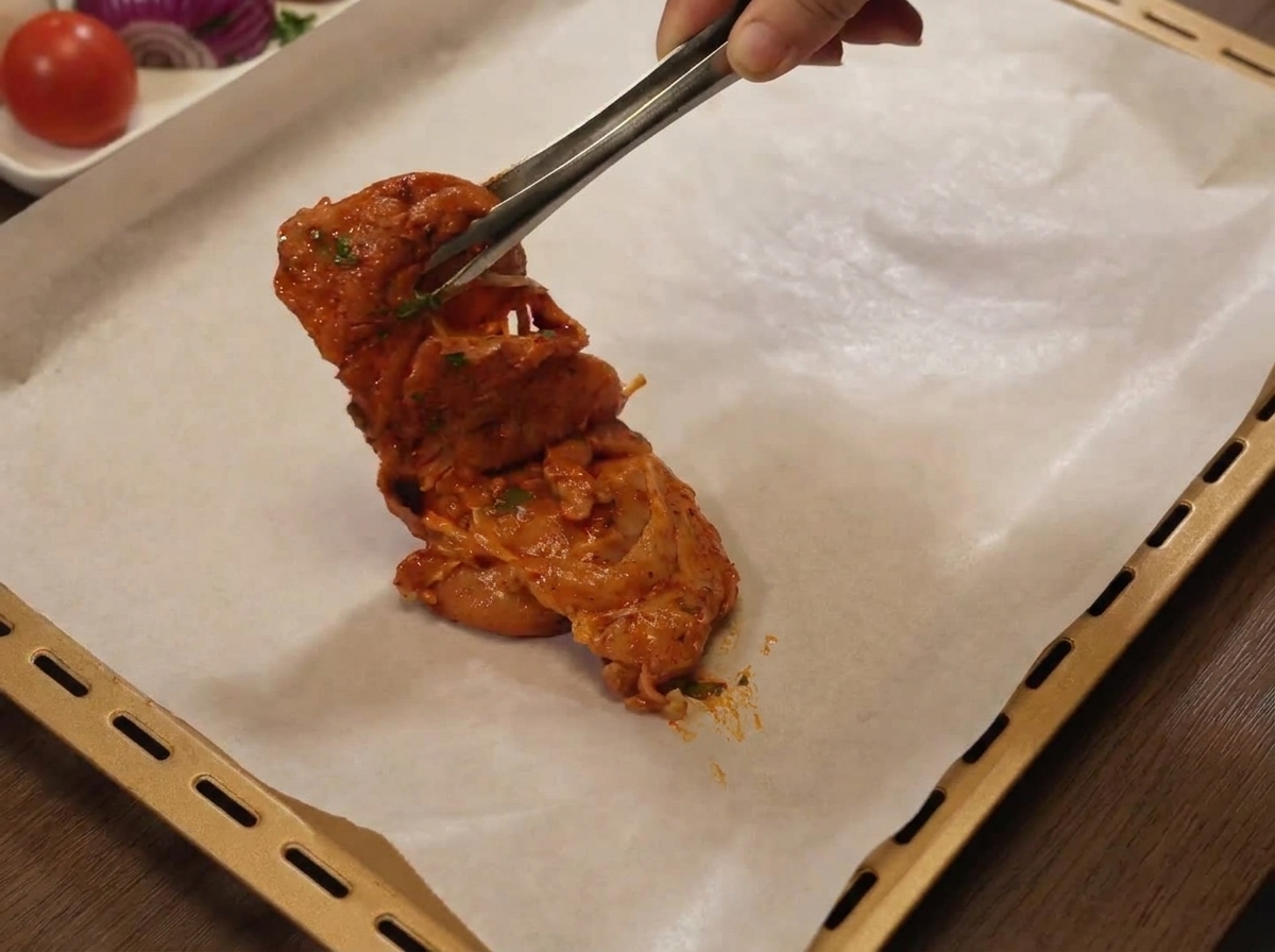Sovracosce di pollo marinate posizionate su una teglia foderata con carta forno.