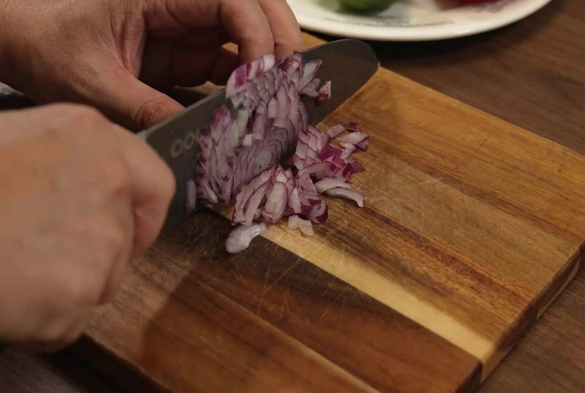 Cipolla rossa finemente tritata su un tagliere di legno con un coltello.