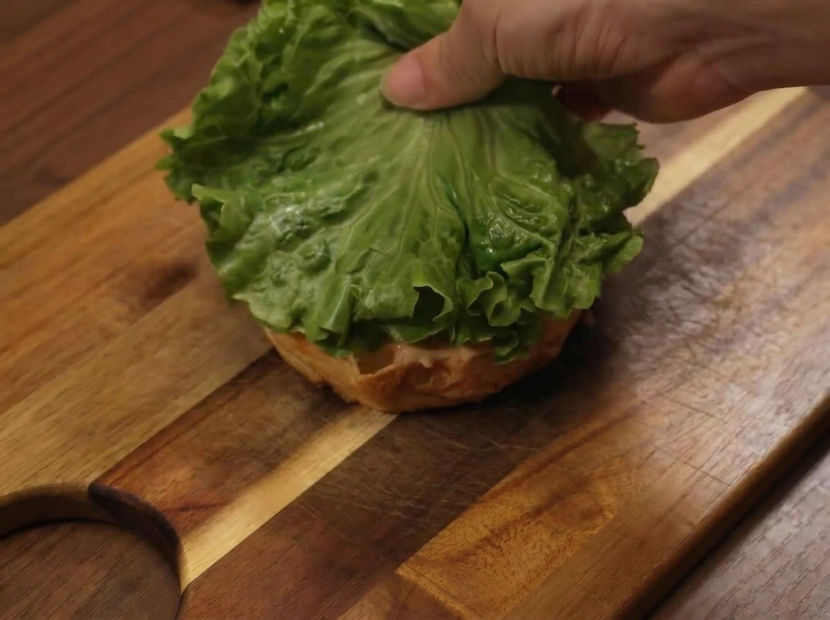 Una foglia di lattuga posizionata sulla base del panino durante lassemblaggio.