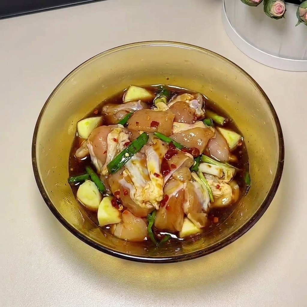 Cosce di pollo crude massaggiate a mano con gli ingredienti della marinata in una ciotola di vetro.