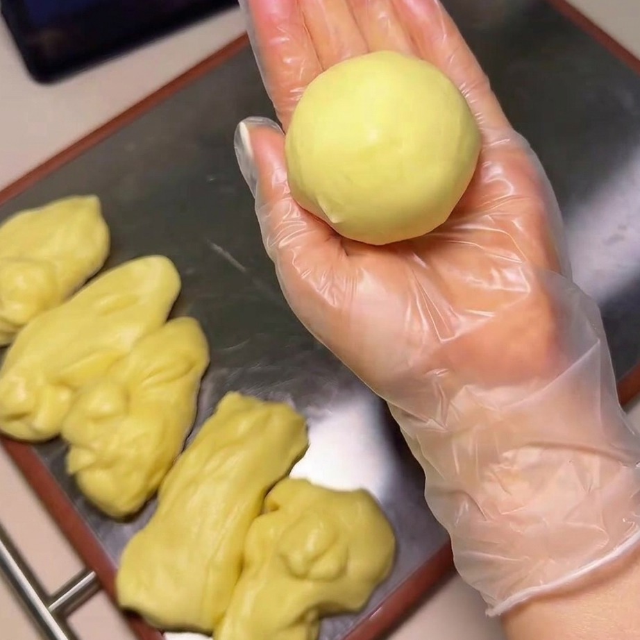 Primo piano di una mano che immerge una pallina di impasto liscia in una ciotola piena di semi di sesamo bianchi.