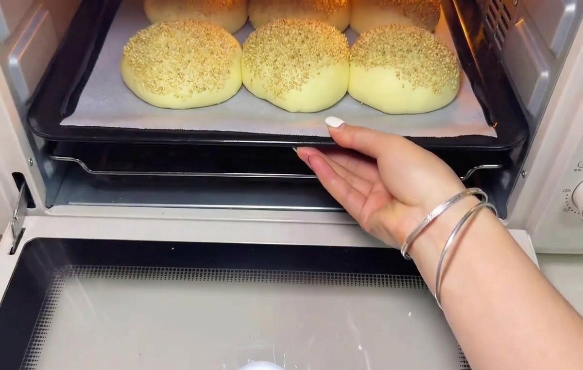 Una teglia di panini lievitati e guarniti con sesamo infornati in un forno preriscaldato.