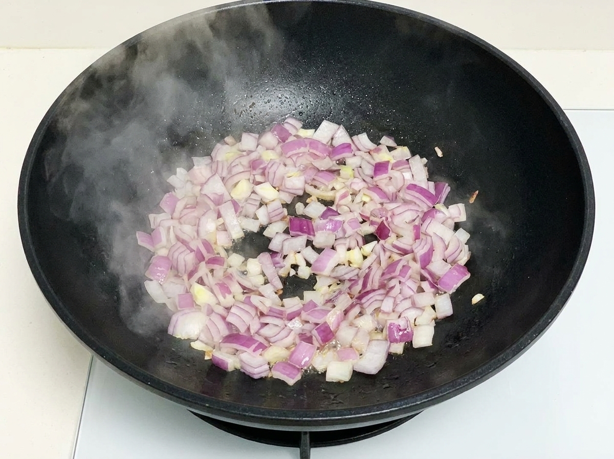 Cipolle rosse tritate che soffriggono in un wok caldo con vapore che sale.