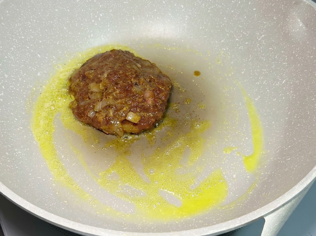 Un hamburger di manzo condito che frigge in una padella a fuoco basso.