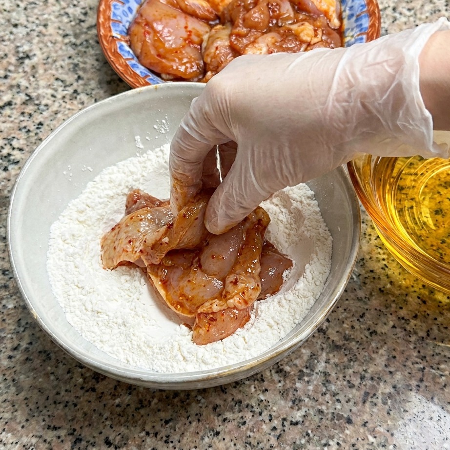 Una coscia di pollo marinata pressata in una ciotola di farina.