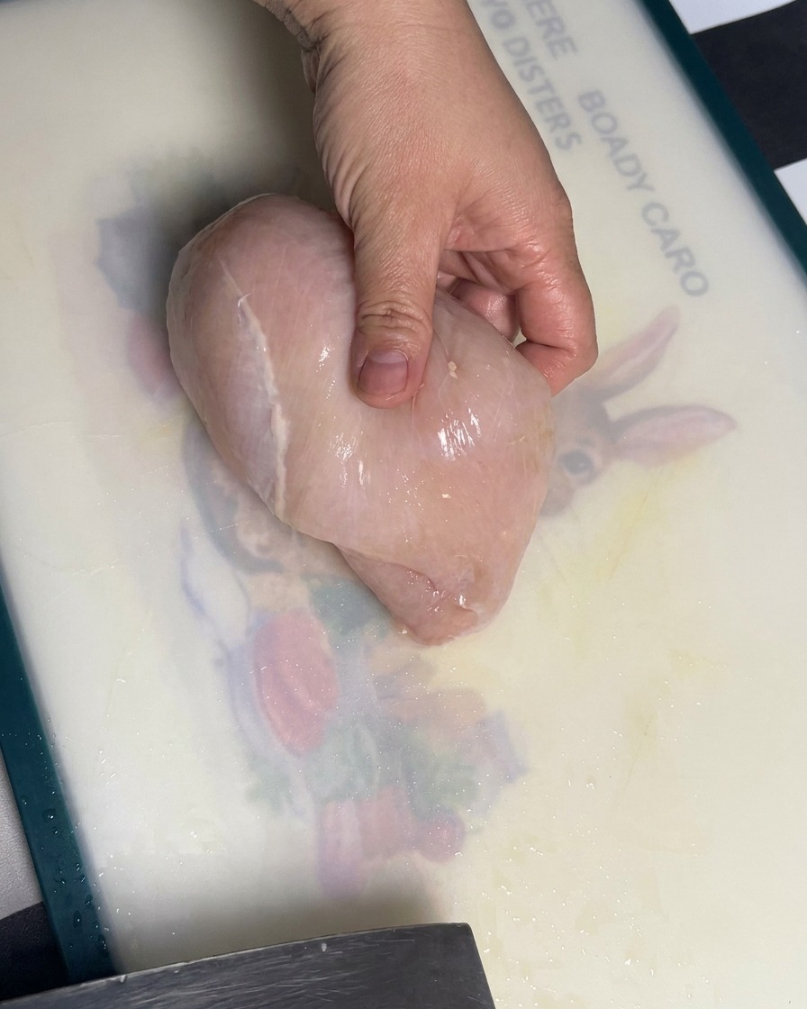 Petti di pollo crudi tagliati in fette uniformi su un tagliere.