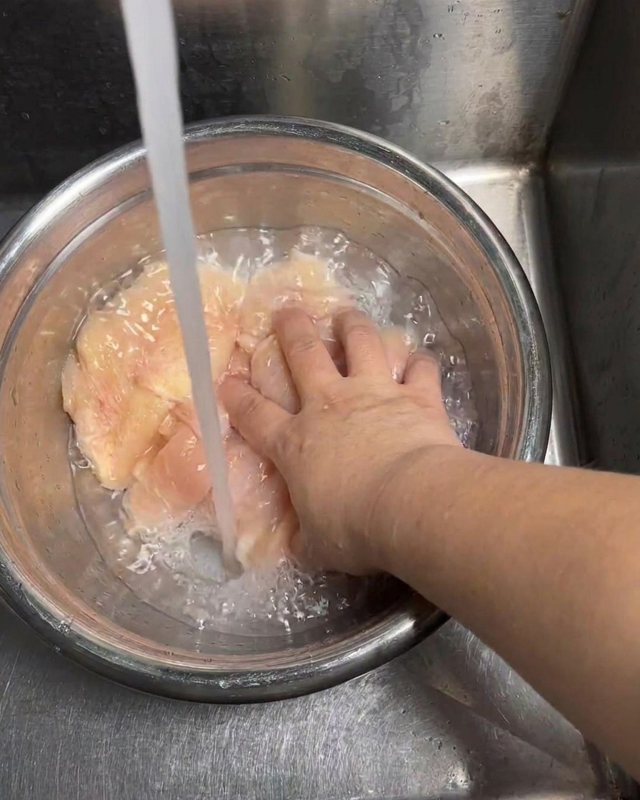 Fette di pollo sciacquate sotto un getto di acqua fredda.