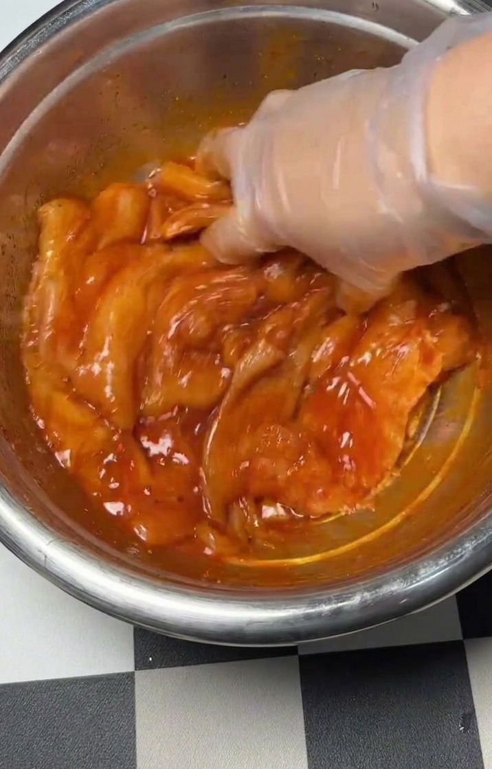 Mano che mescola il pollo condito e la marinata in una ciotola.