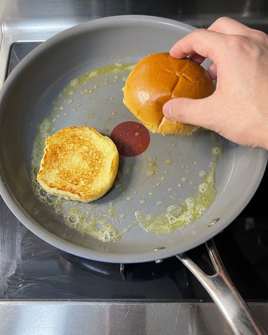 Panini da hamburger in padella con burro fuso, durante la tostatura.