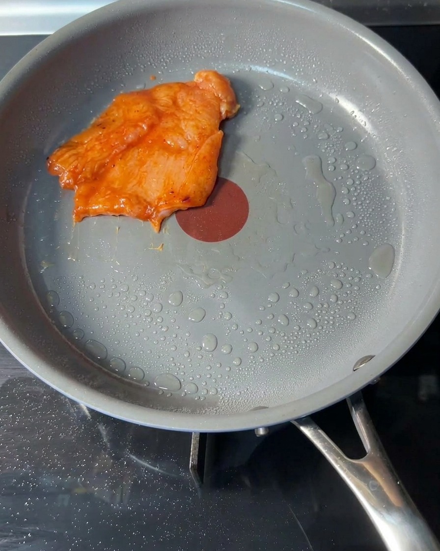 Burger di pollo crudi marinati posizionati in una padella calda con un velo dolio.