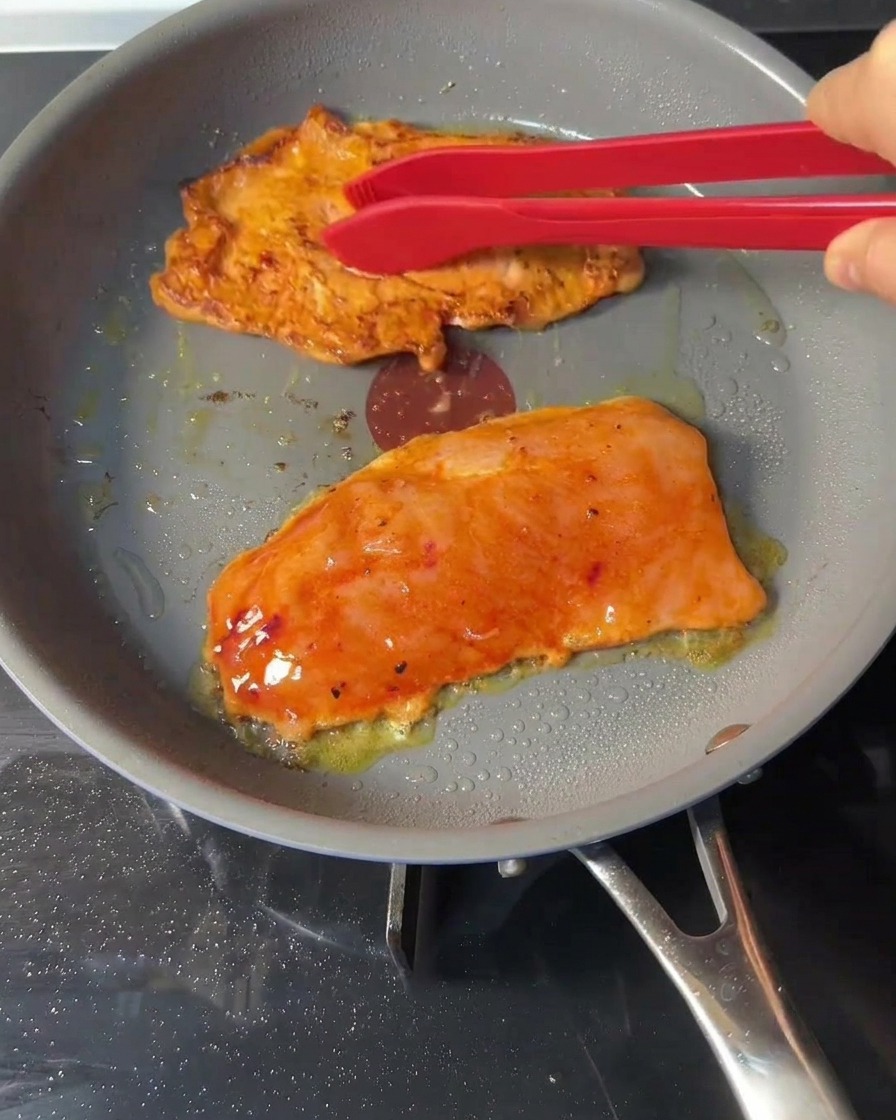 Pinze in silicone rosse che girano i burger di pollo dorati in padella.