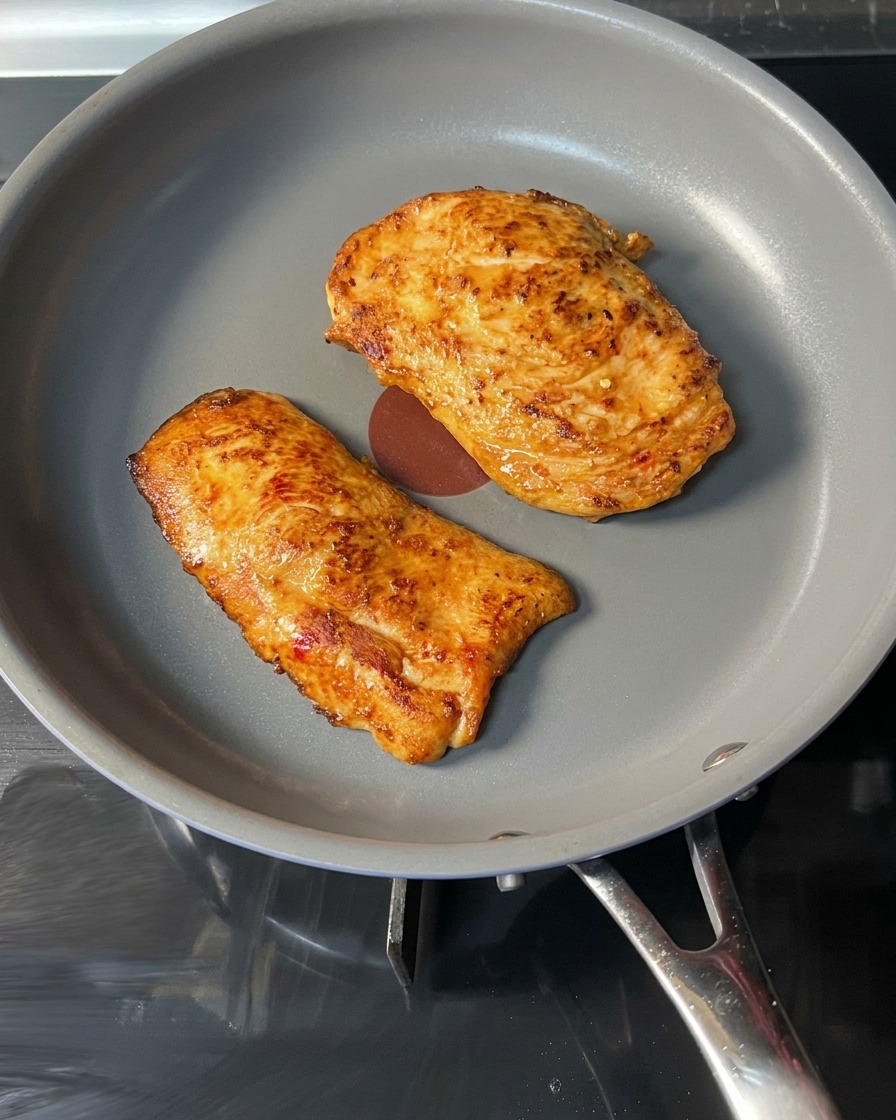 Un burger di pollo cotto e dorato sollevato da una padella con le pinze.