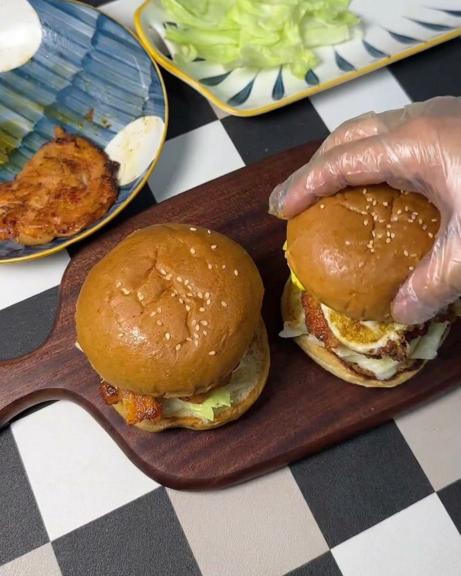 Una mano che posiziona il pane superiore sopra luovo e il pollo per chiudere il sandwich.