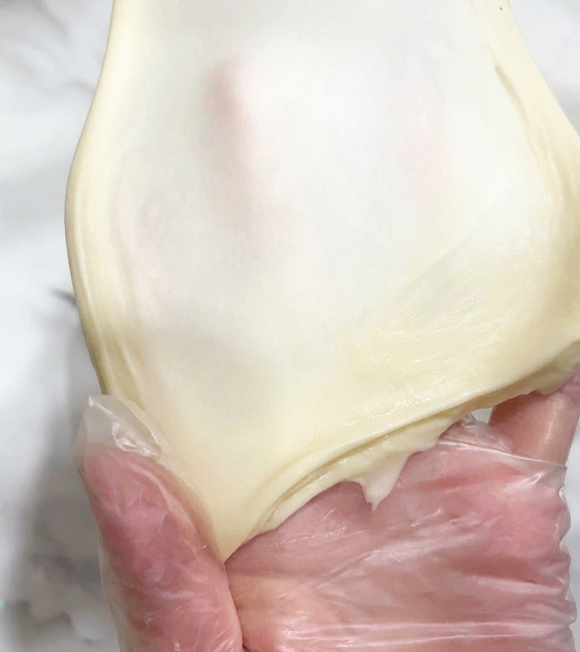Un pezzo di impasto liscio ed elastico teso sottilmente a mano per mostrare la luce che passa attraverso.