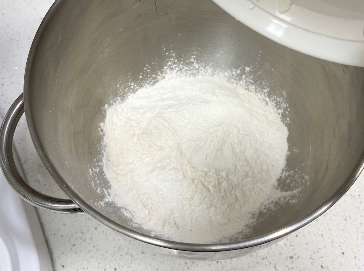Farina secca e ingredienti allinterno della ciotola di unimpastatrice planetaria pulita.