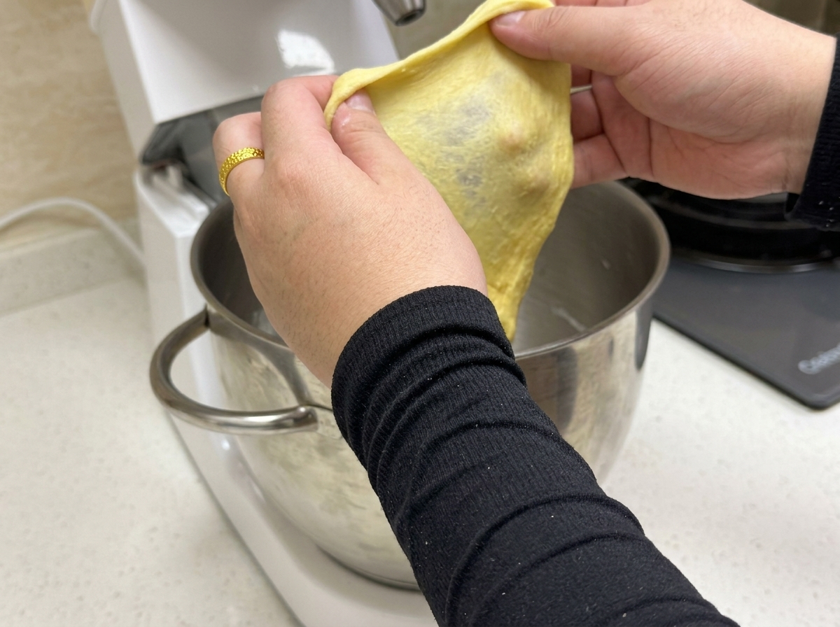 Una piccola porzione di impasto giallo steso per mostrare una sottile membrana elastica di glutine.
