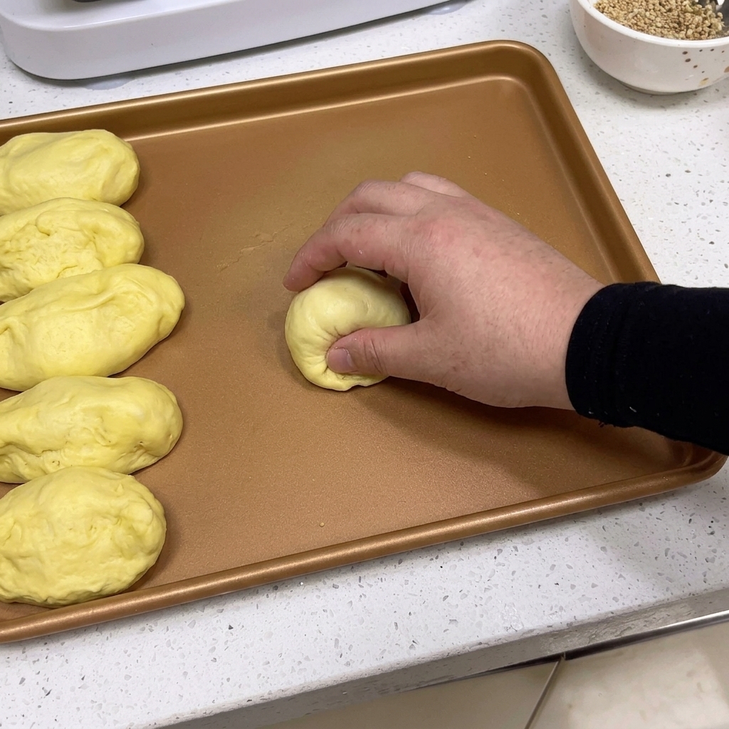 Mani che modellano una porzione di impasto in una pallina liscia e rotonda su un vassoio.