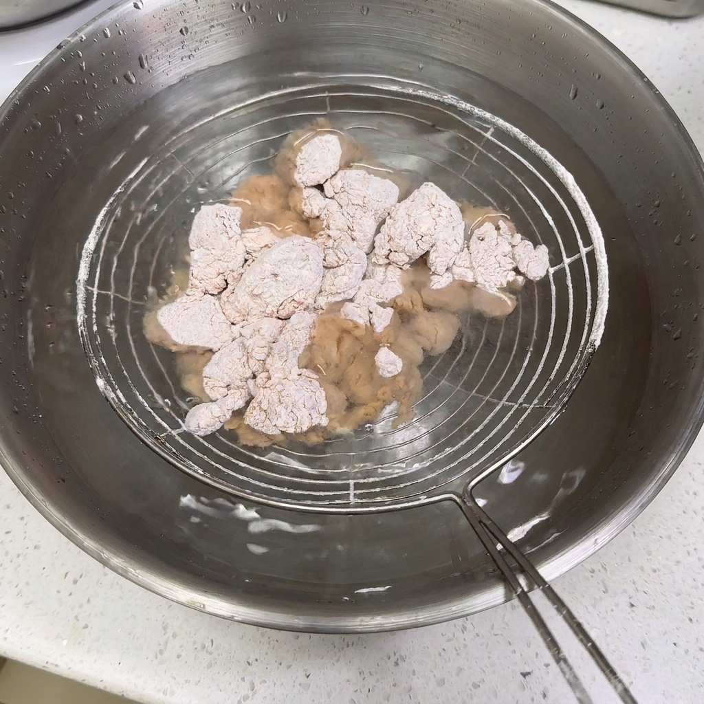 Pezzi di pollo rivestiti di farina immersi in una ciotola di acciaio inossidabile piena dacqua su una schiumarola.