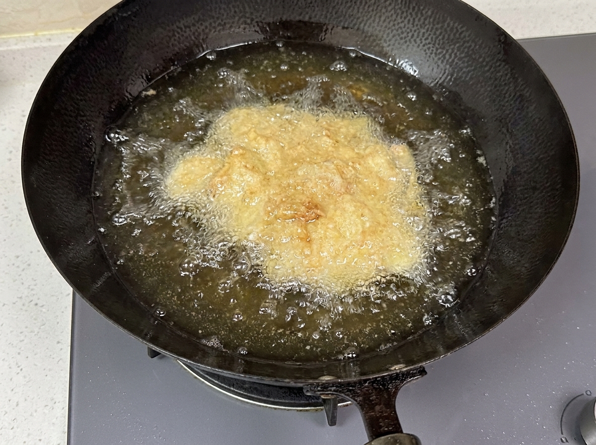 Pezzi di pollo impanato che sfrigolano nellolio caldo dentro un wok scuro.