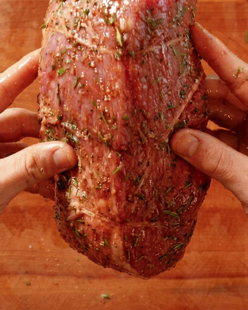 Mani che mettono un arrosto di manzo crudo condito in una padella rovente.