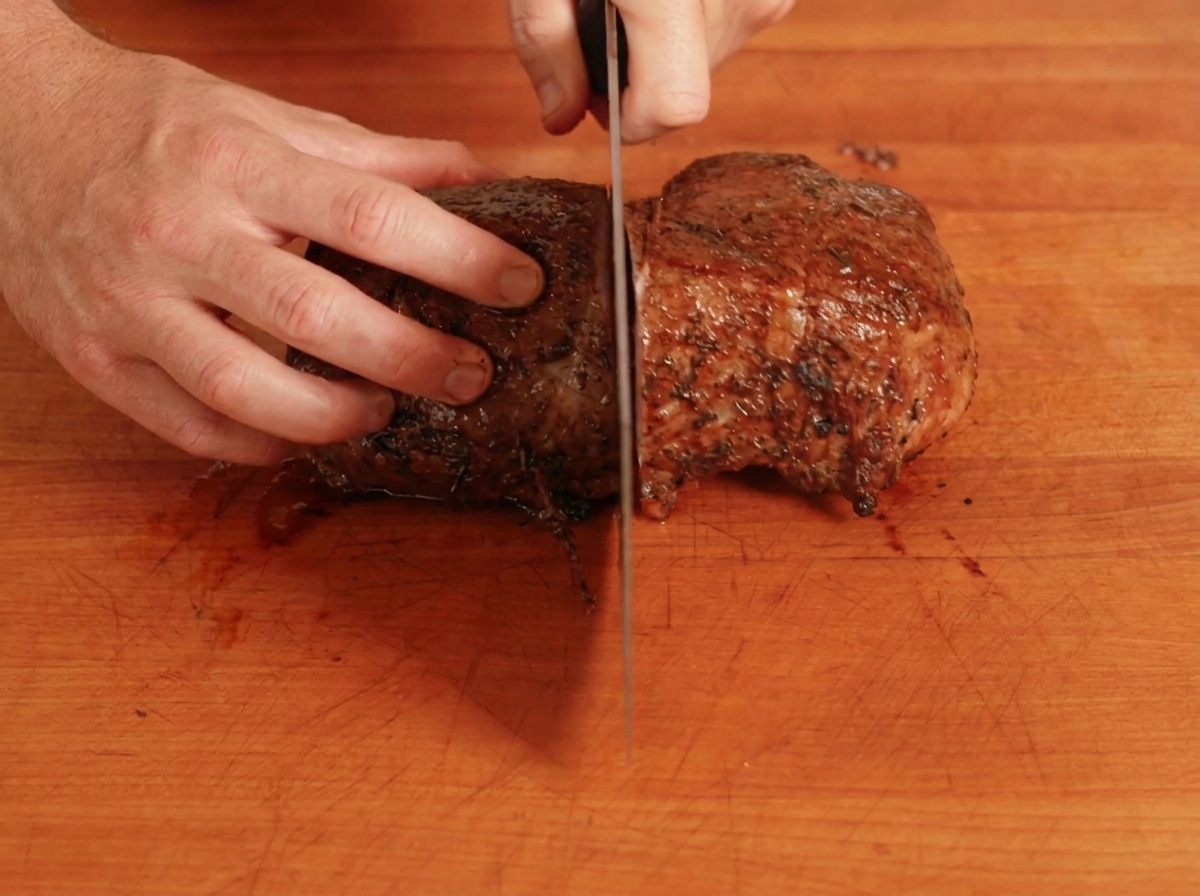 Un arrosto di manzo cotto tagliato a metà su un tagliere di legno.