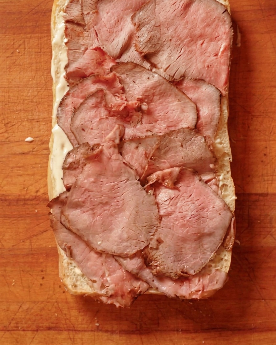 Manzo arrosto cotto a fette sottili disposto su uno strato di crema su un pezzo di pane.