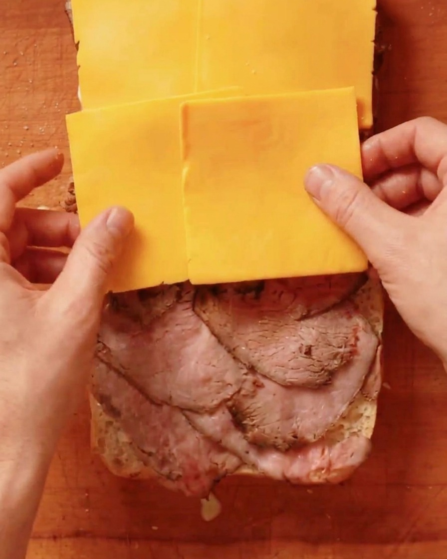 Fette di formaggio cheddar giallo posizionate sopra uno strato di roast beef.