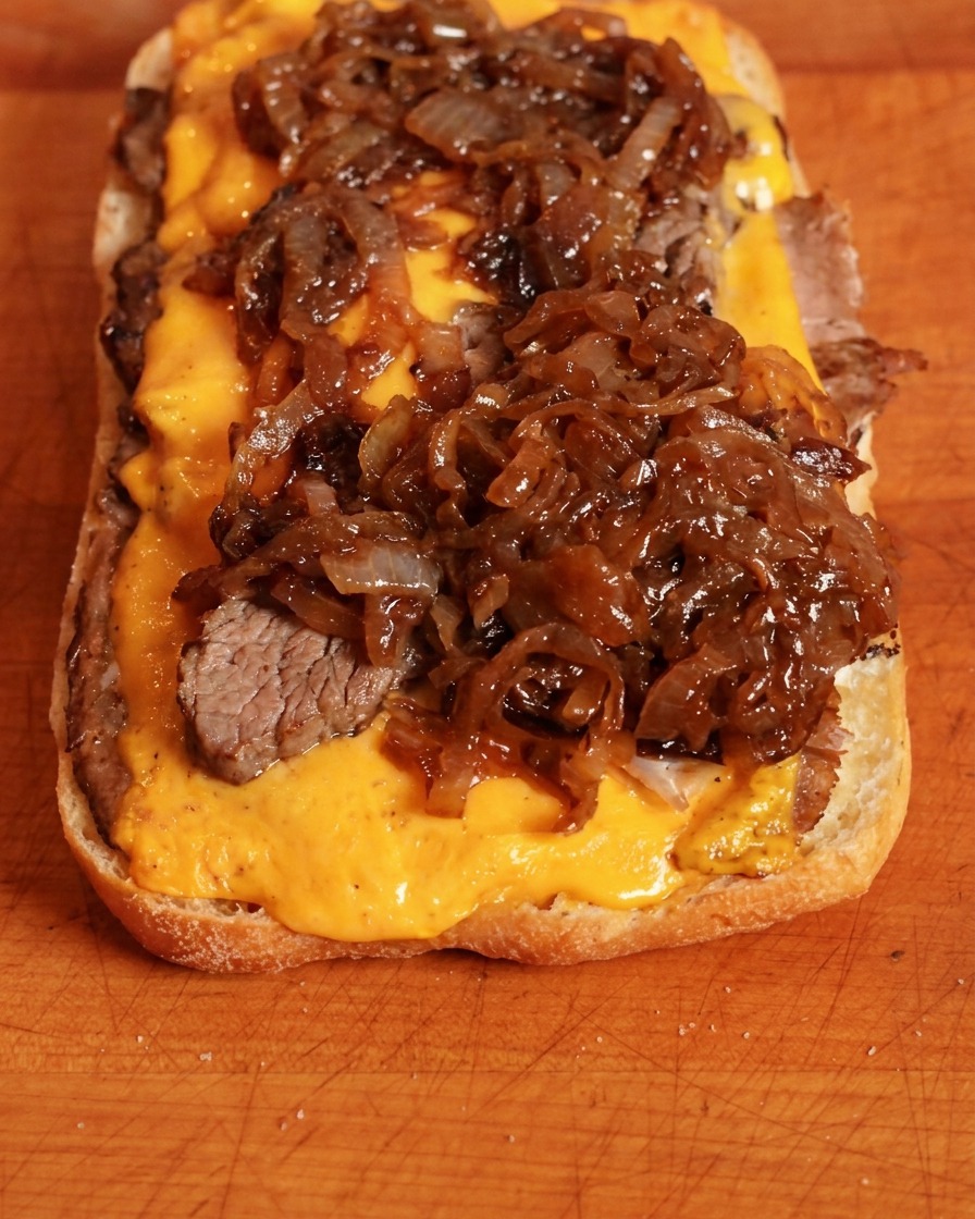 Cipolle caramellate ricche e scure messe sopra il formaggio cheddar su una base di panino.