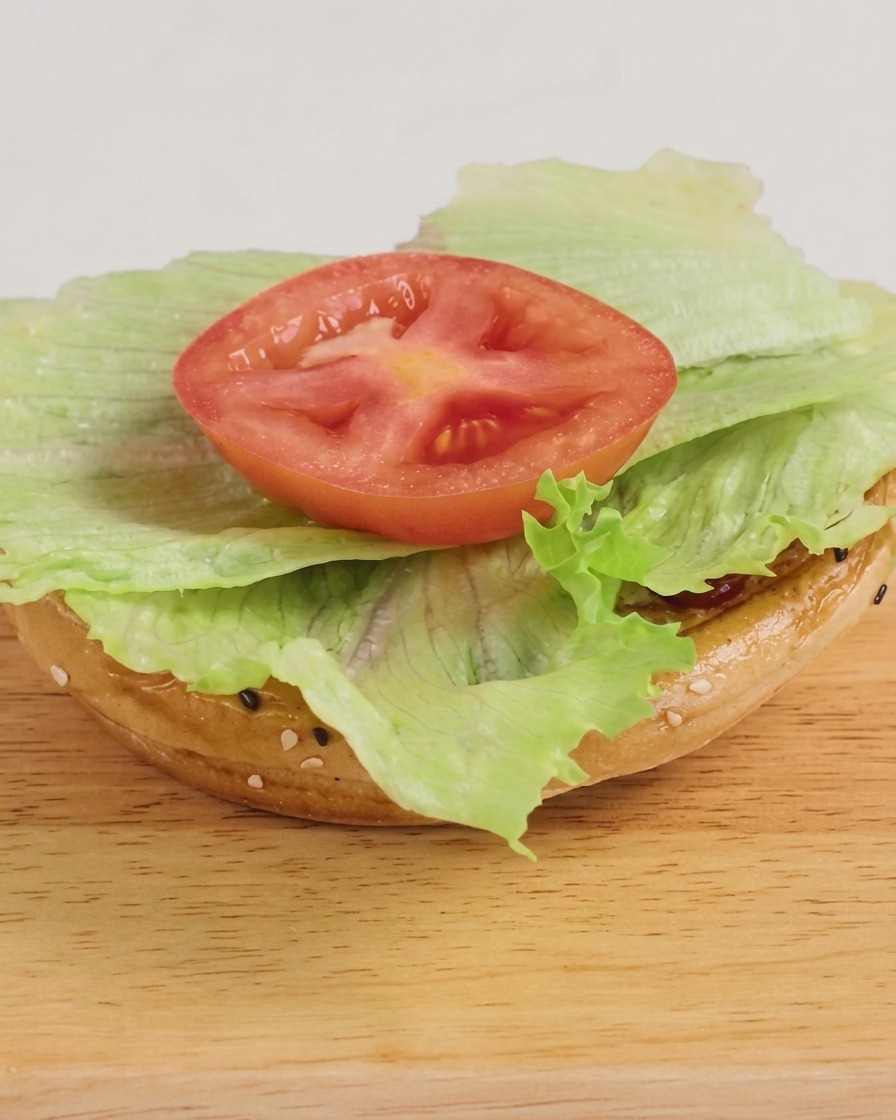 Un hamburger appena assemblato con lattuga, hamburger al formaggio e una pioggia di salsa BBQ, pronto per essere servito.