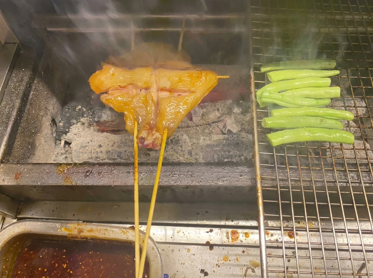 Cosce di pollo e fagiolini che cuociono sulla brace su una griglia metallica.