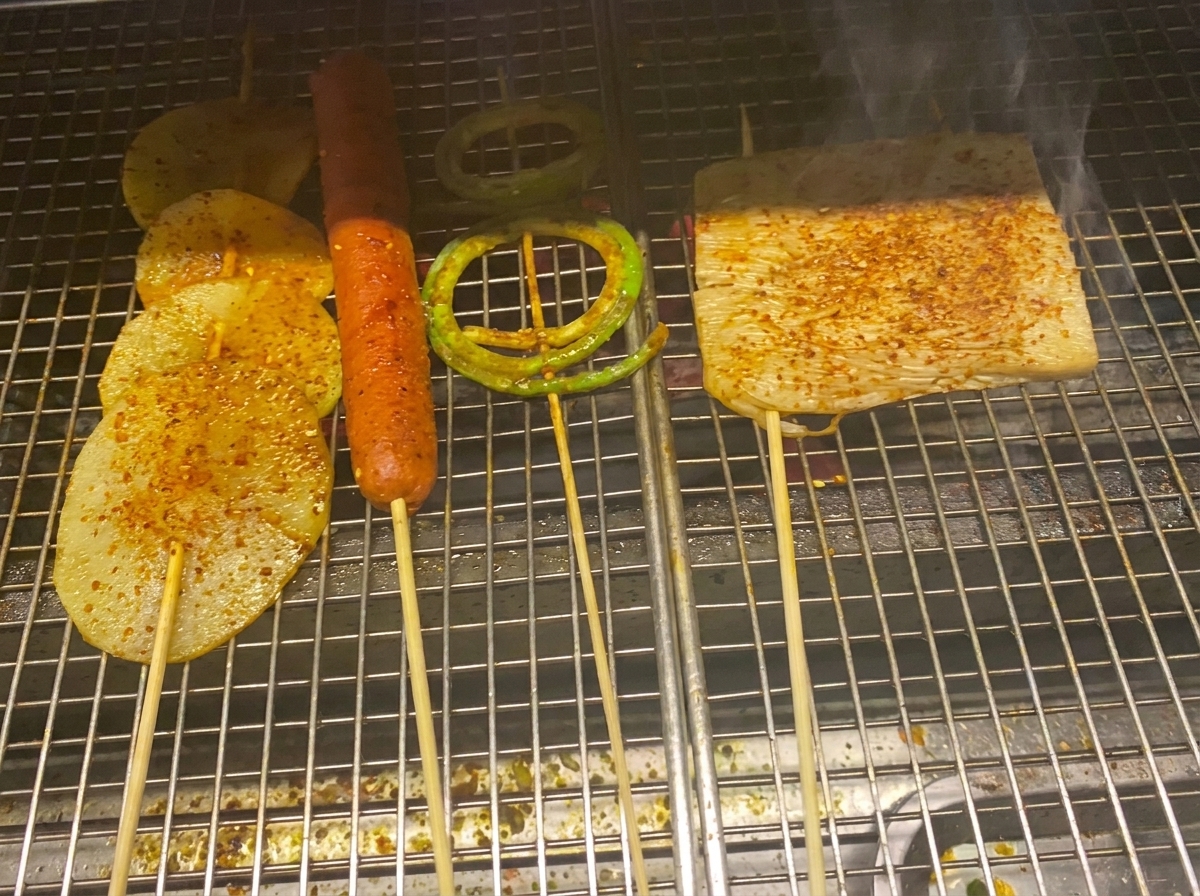 Fette di patata grigliate, salsiccia e verdure ricoperte di salsa barbecue lucida e scaglie di peperoncino.