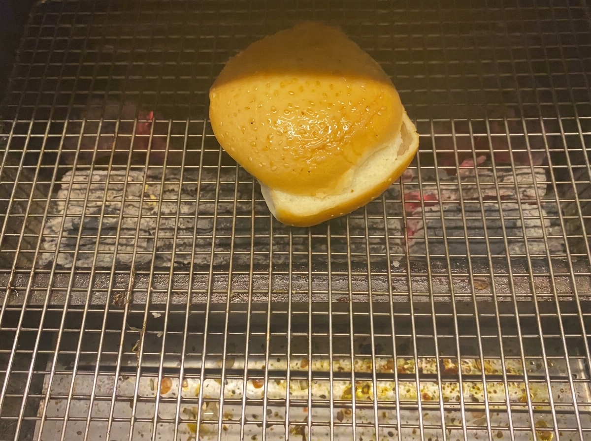 Una metà di un panino da burger che tosta rivolta verso il basso sulla griglia.
