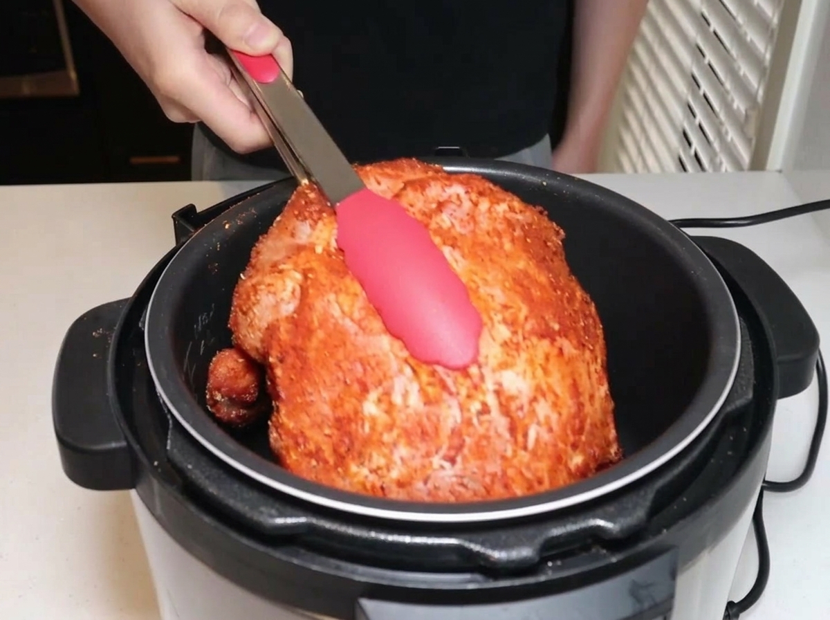 Spalla di maiale condita inserita in una pentola a pressione elettrica con le pinze.