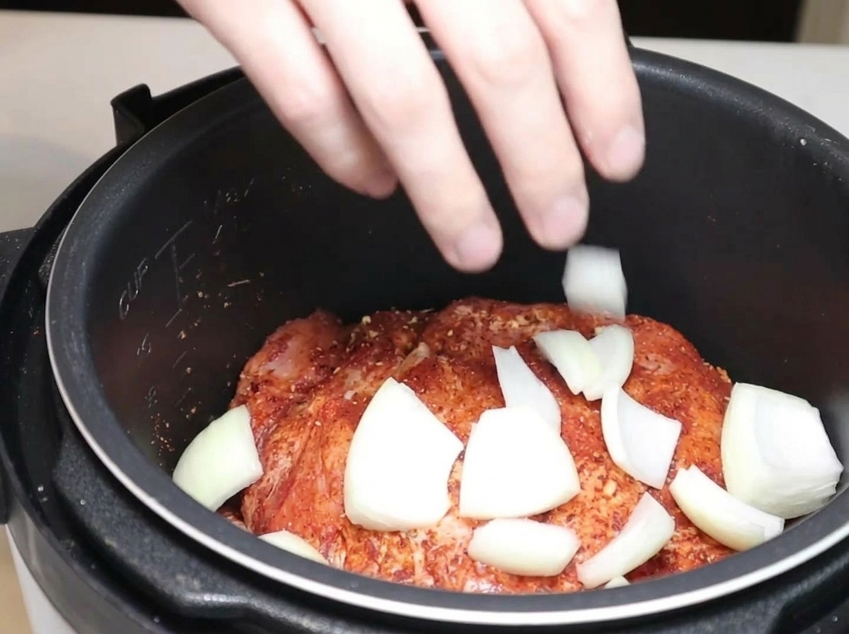 Spicchi di cipolla e peperoncini secchi inseriti nella pentola a pressione con il maiale.