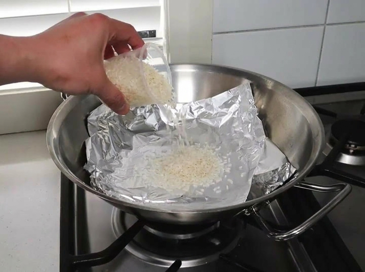 Riso crudo e trucioli di legno distribuiti uniformemente su un wok foderato di alluminio.