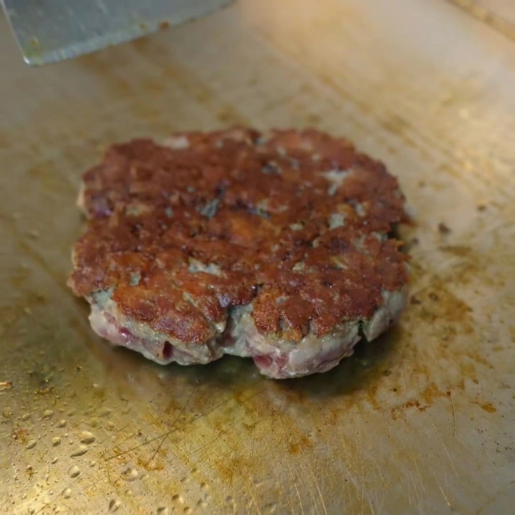 Una fetta di formaggio giallo che si scioglie su un hamburger di manzo rosolato sotto una cupola di metallo.