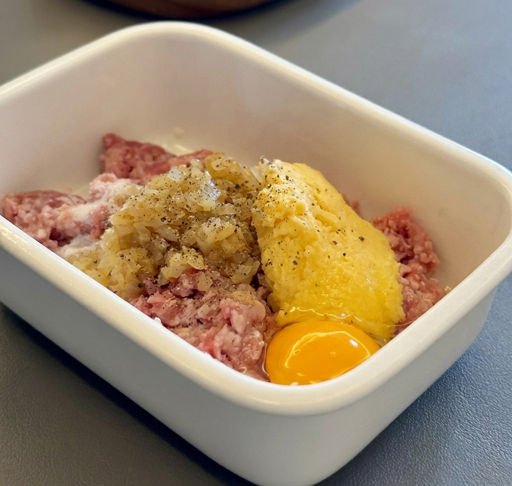 Ingredienti per le polpette Hamburg uniti in un contenitore bianco.