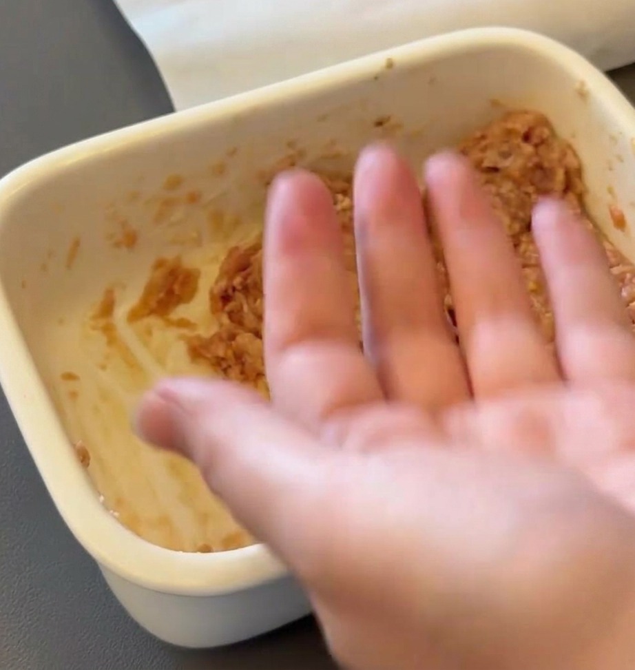 Una mano che modella il composto di carne macinata cruda a forma di polpetta rotonda.