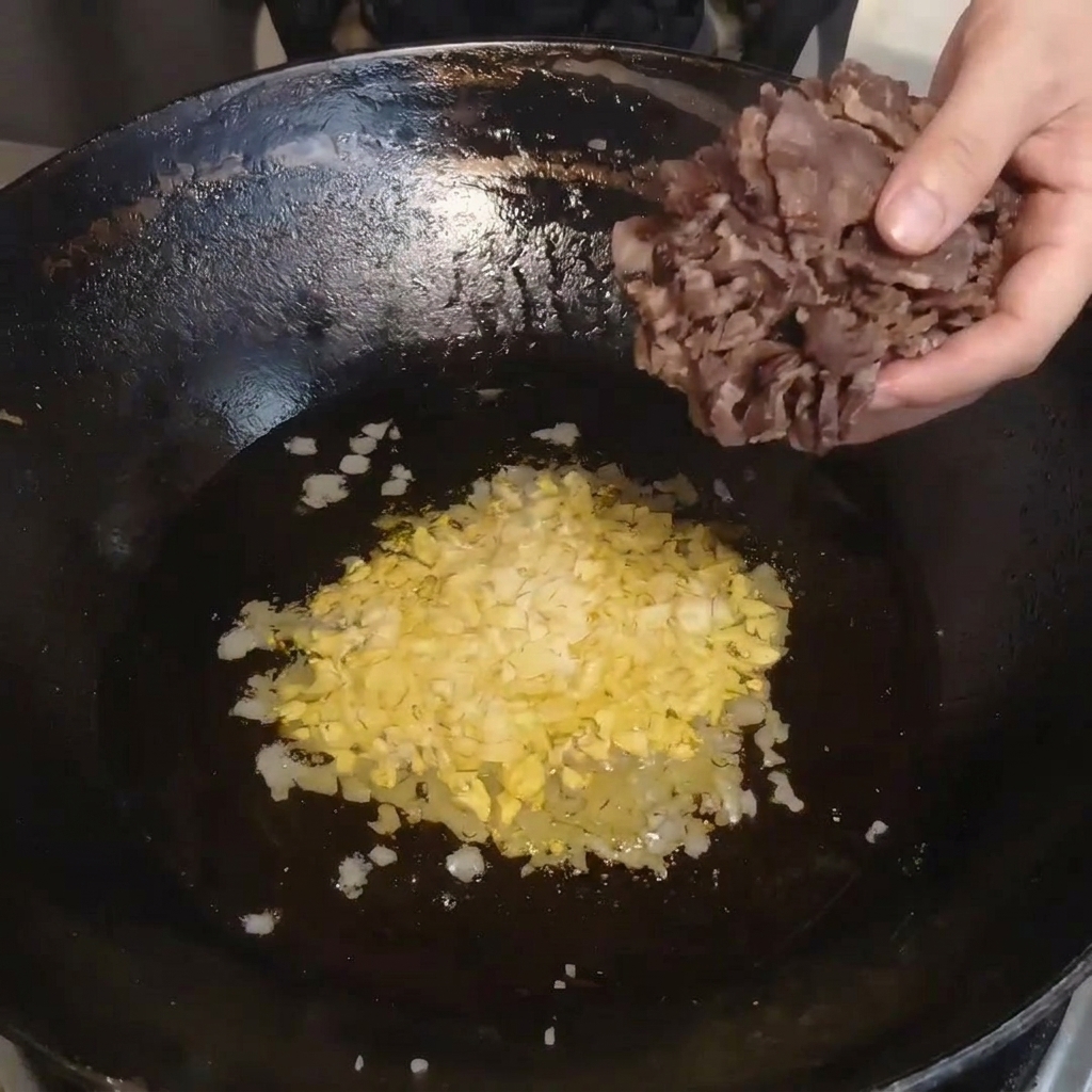 Fette di carne essiccata cotte al vapore trasferite da una ciotola in un wok caldo.